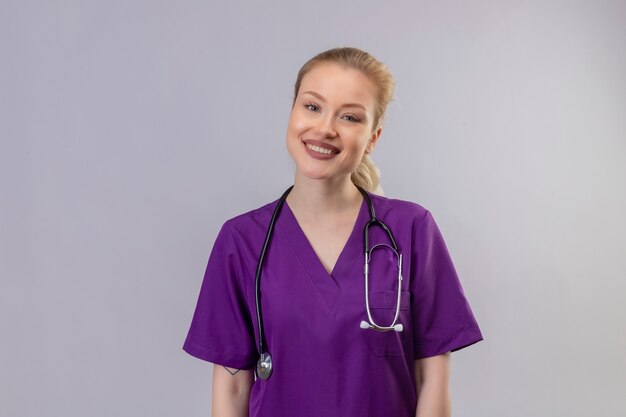 Glimlachende jonge arts die purpere medische toga en stethoscoop op geïsoleerde witte muur draagt