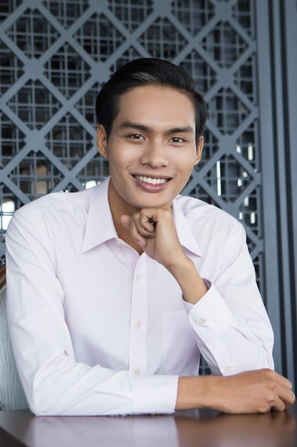 Gratis foto glimlachende jonge aziatische man zit in restaurant