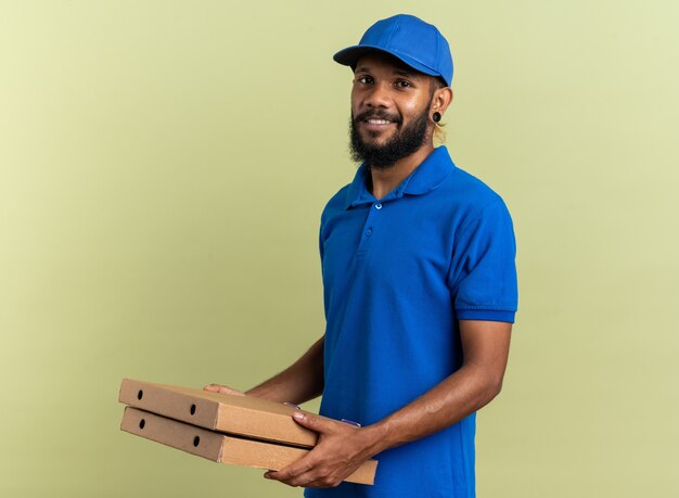 Glimlachende jonge bezorger met pizzadozen geïsoleerd op olijfgroene muur met kopieerruimte