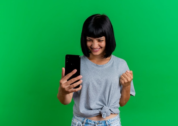 Glimlachende jonge brunette blanke vrouw houdt vuist naar de telefoon te kijken