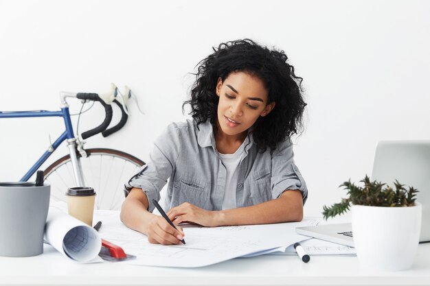 Glimlachende jonge donkere zelfstandige vrouw architect met Afro kapsel tekening maken