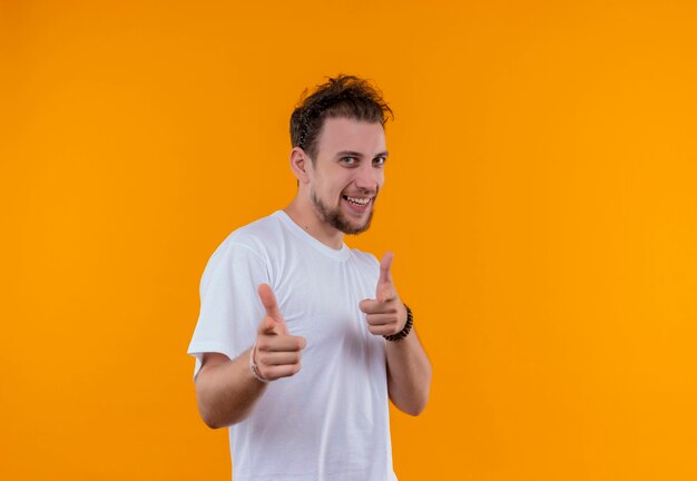 Glimlachende jonge kerel die wit t-shirt draagt die u gebaar op geïsoleerde oranje achtergrond toont