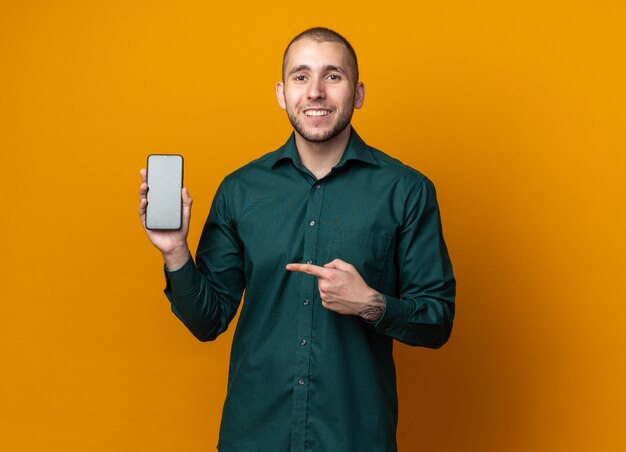 Glimlachende jonge knappe kerel die een groen shirt draagt en naar de telefoon wijst