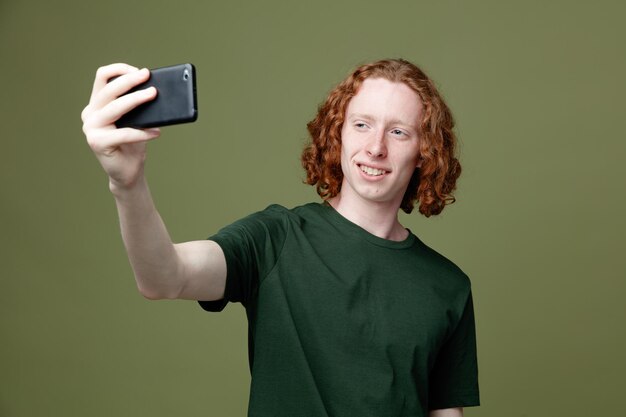 Glimlachende jonge knappe kerel met een groen t-shirt neemt een selfie geïsoleerd op een groene achtergrond
