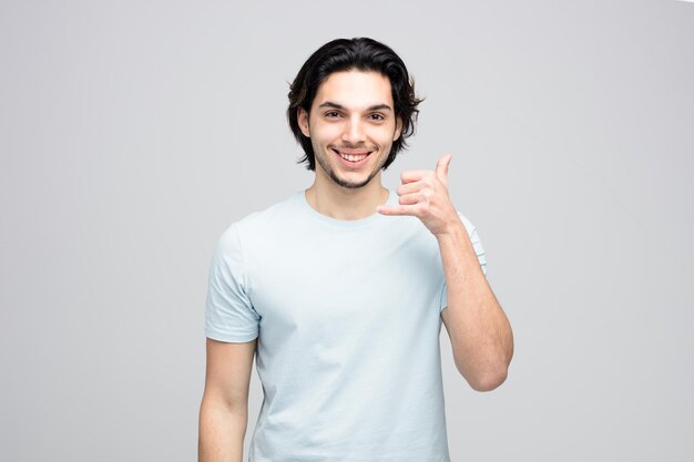 Glimlachende jonge knappe man die naar de camera kijkt en een los gebaar laat zien dat op een witte achtergrond wordt geïsoleerd