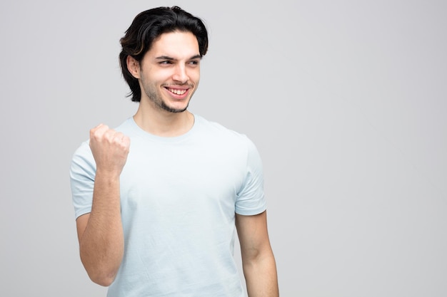 Glimlachende jonge knappe man die naar de zijkant kijkt en een ja-gebaar toont dat op een witte achtergrond met kopieerruimte wordt geïsoleerd