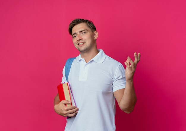 Glimlachende jonge knappe mannelijke student die de boeken van de achterzakholding draagt