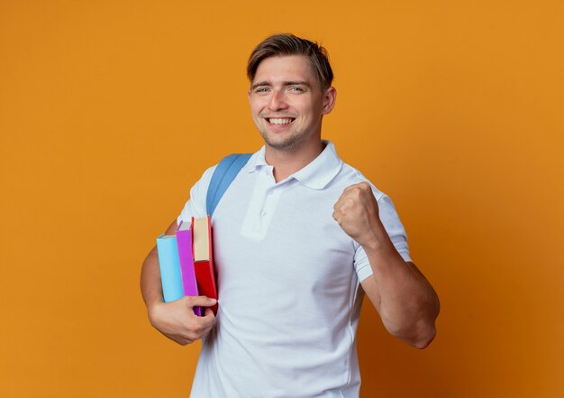 Glimlachende jonge knappe mannelijke student die de boeken van de achterzakholding draagt