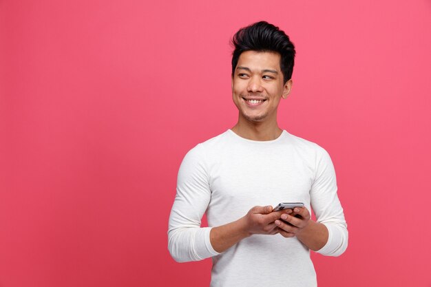 Glimlachende jonge man die mobiele telefoon houdt die kant bekijkt