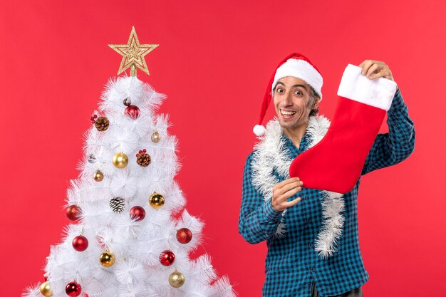 Glimlachende jonge man met kerstman hoed in een blauw gestript shirt en kerst sok te houden