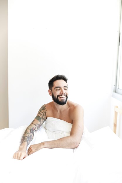 Glimlachende jonge man zittend op bed