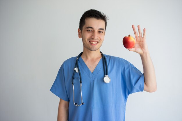 Glimlachende jonge mannelijke arts die en appel tonen aanbevelen.