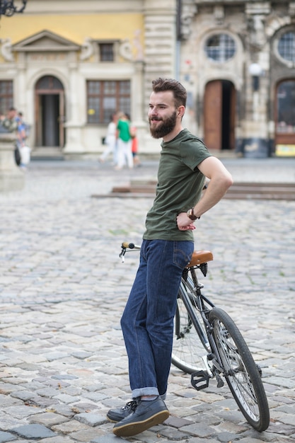 Gratis foto glimlachende jonge mannelijke fietser met fiets op straat