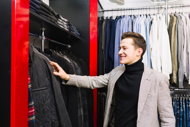 Glimlachende jonge mens die de kleren in het rek controleert