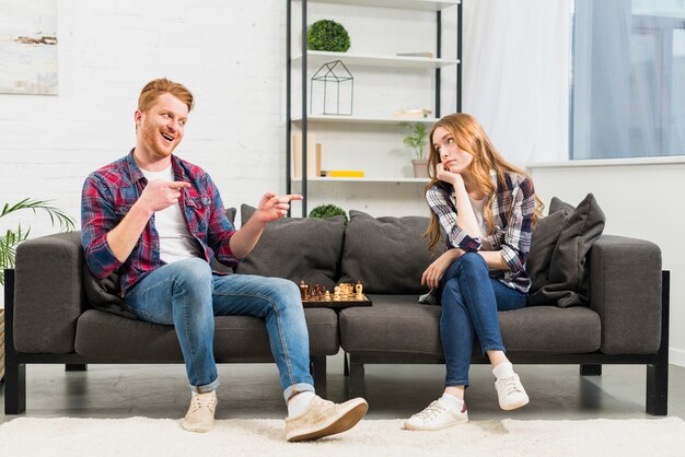 Glimlachende jonge mens die pret van haar meisje na het winnen van het schaakspel in de woonkamer maken