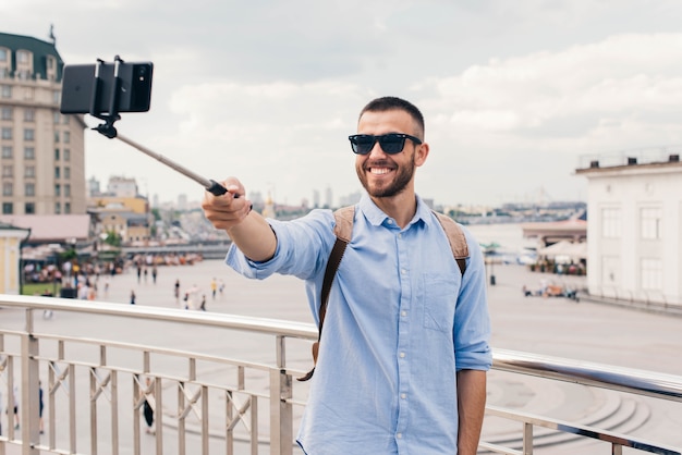Glimlachende jonge mens die zonnebril dragen die selfie met smartphone nemen