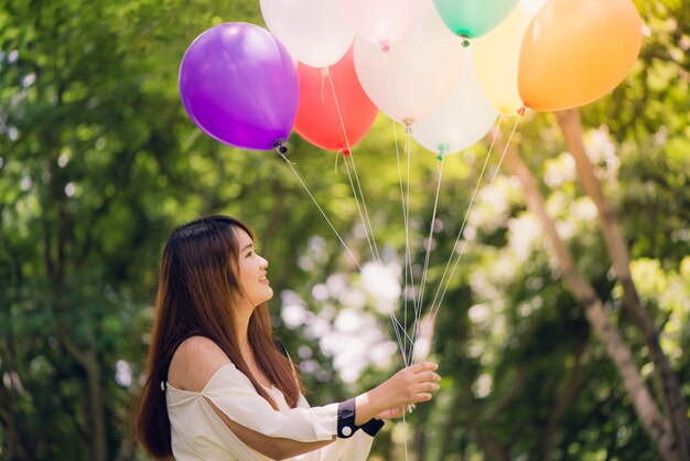 Glimlachende jonge mooie Aziatische vrouwen met lang bruin haar in het park. Met regenboogkleurige luchtballonnen in haar handen. Zonnige en positieve energie van de natuur.
