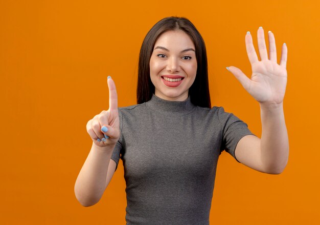 Glimlachende jonge mooie vrouw die één en vijf met handen toont die op oranje achtergrond worden geïsoleerd