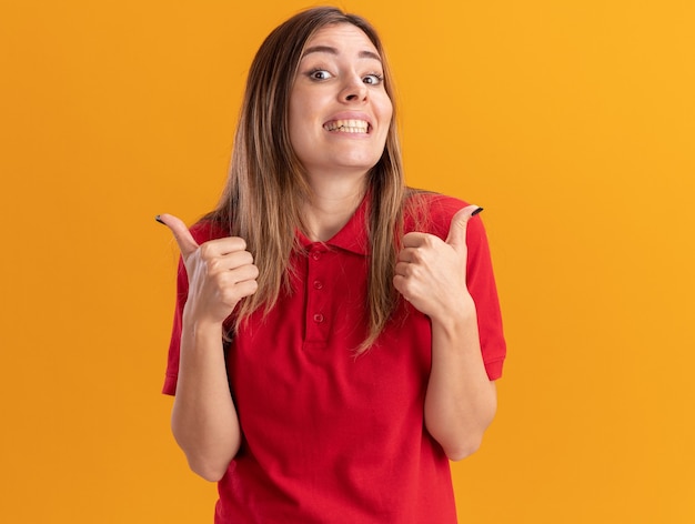 Glimlachende jonge mooie vrouw thumbs up van twee handen geïsoleerd op oranje muur