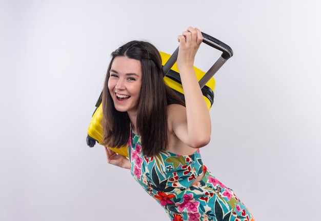 Glimlachende jonge reizigersvrouw die veelkleurige kleding draagt die een gsm op haar schouder op witte muur houdt