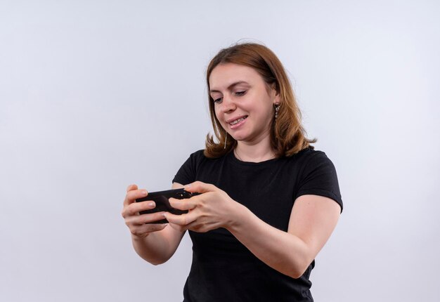 Glimlachende jonge toevallige vrouw die mobiele telefoon houdt en bekijkt op geïsoleerde witte ruimte met exemplaarruimte