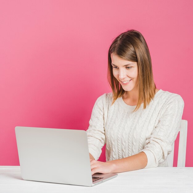 Glimlachende jonge vrouw die aan laptop voor roze muur werkt