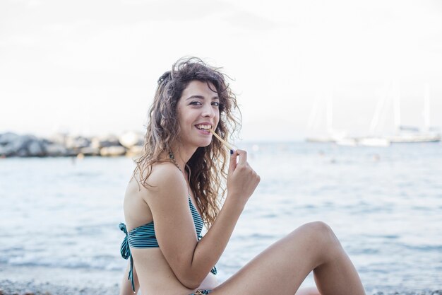 Glimlachende jonge vrouw die broodstok eten bij strand