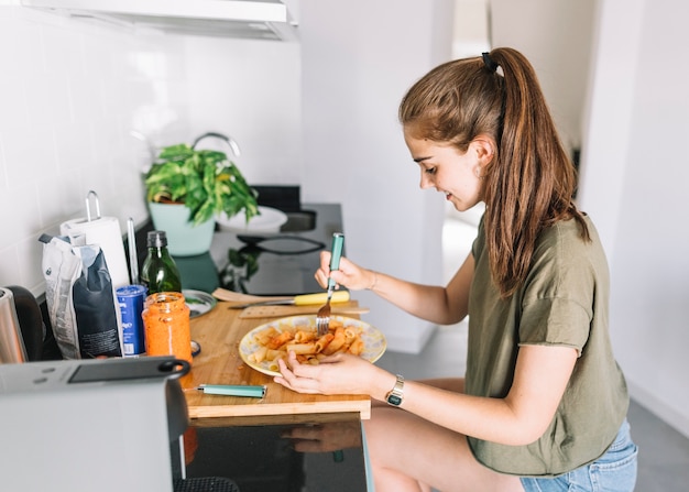 Glimlachende jonge vrouw die deegwaren in ontbijt eet