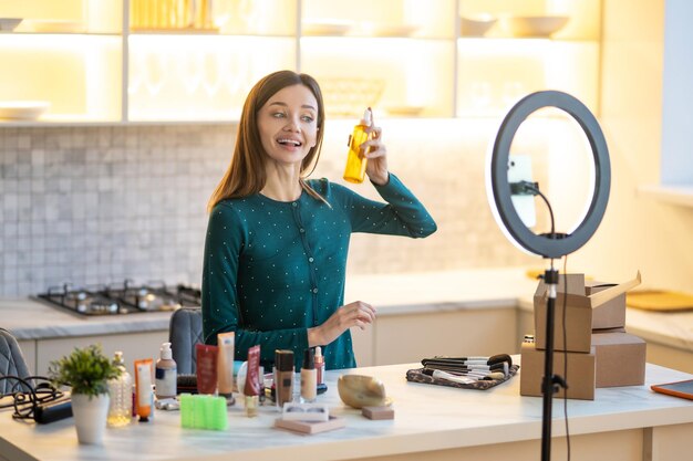 Glimlachende jonge vrouw die haarlak voorstelt tijdens online beauty-tutorial