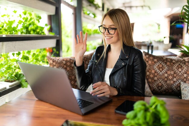 Glimlachende jonge vrouw die laptop gebruikt en videogesprek voert in café.