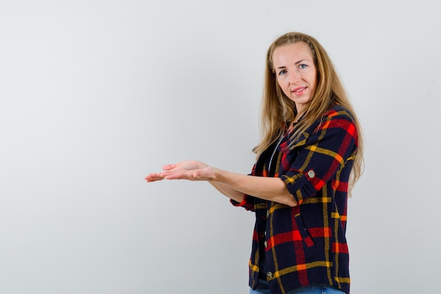 Glimlachende jonge vrouw die links met handen op witte achtergrond toont