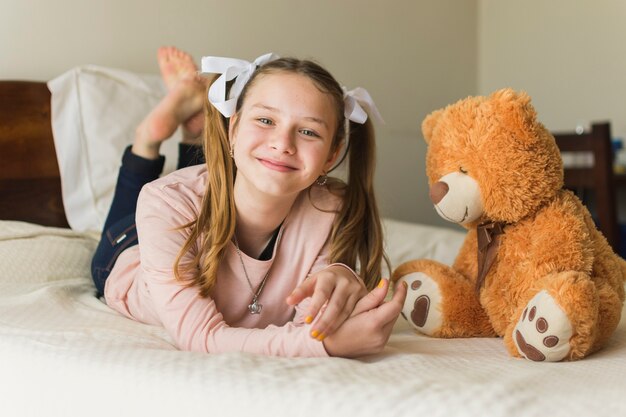 Glimlachende jonge vrouw die op bed met teddybeer ligt