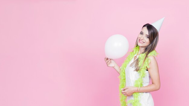 Glimlachende jonge vrouw die partijhoed draagt ​​die witte ballon houdt