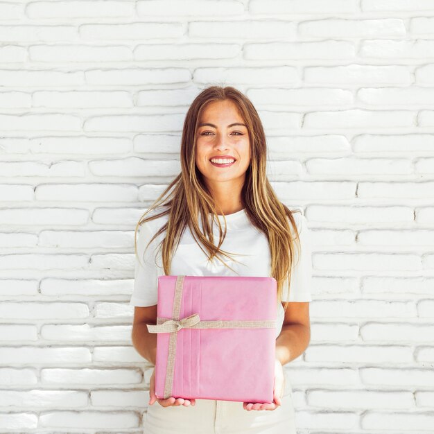 Glimlachende jonge vrouw die roze giftdoos houdt