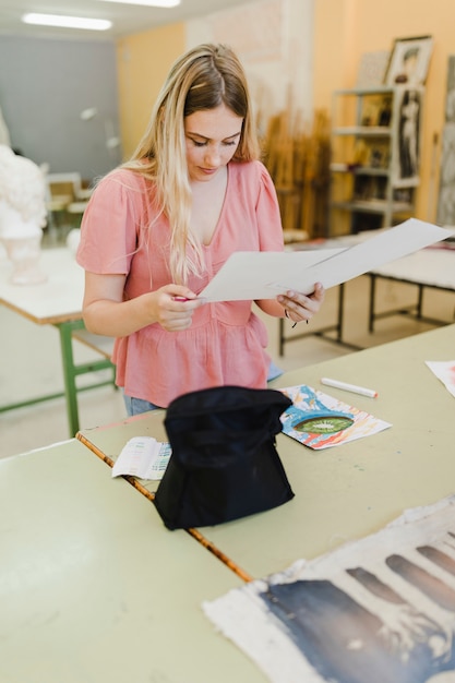 Gratis foto glimlachende jonge vrouw die schilderijen in de workshop bekijkt