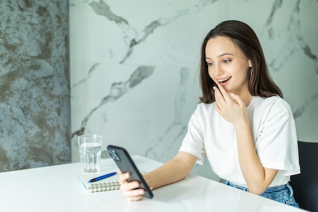 Glimlachende jonge vrouw die slimme telefoon in keuken met behulp van. vrouw scroll door het sociale netwerk