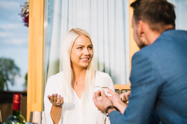 Gratis foto glimlachende jonge vrouw die terwijl zijn vriend ophaalt die haar verlovingsring geeft