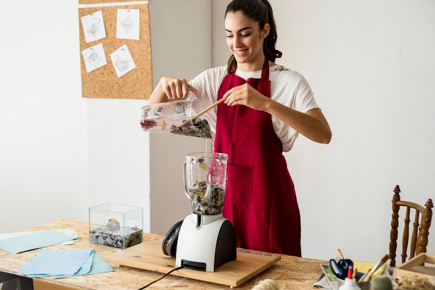 Glimlachende jonge vrouw die voorbereiding voor het malen van document stukken in mixer maakt