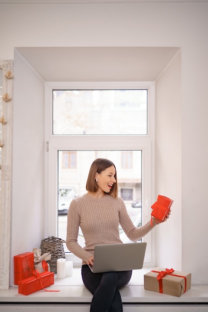 Glimlachende jonge vrouw die vrienden met Kerstmis groet in videochat op laptop met giftdozen