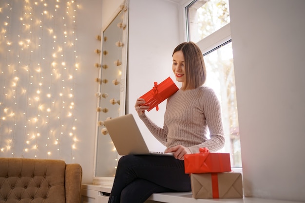 Glimlachende jonge vrouw die vrienden met Kerstmis groet in videochat op laptop met giftdozen