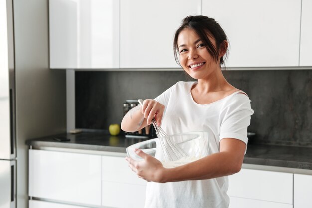 Glimlachende jonge vrouw die zich bij de keuken in huis bevindt