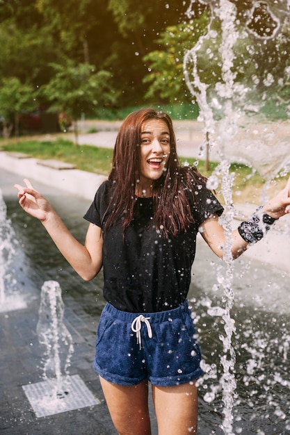 Gratis foto glimlachende jonge vrouw die zich dichtbij fontein bevindt die handgebaar maakt