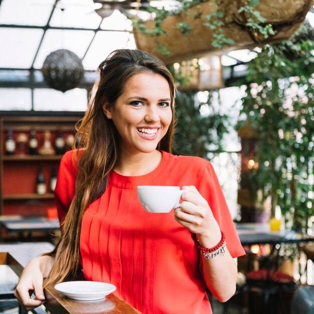 Glimlachende jonge vrouw het drinken kop van koffie in caf�