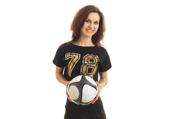 Glimlachende jonge vrouw in een zwart t-shirt ziet er recht uit en houdt de bal geïsoleerd op een witte achtergrond Premium Foto