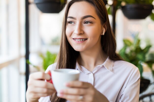 Glimlachende jonge vrouw in het café met koptelefoon luisteren naar muziek of praten over de telefoon