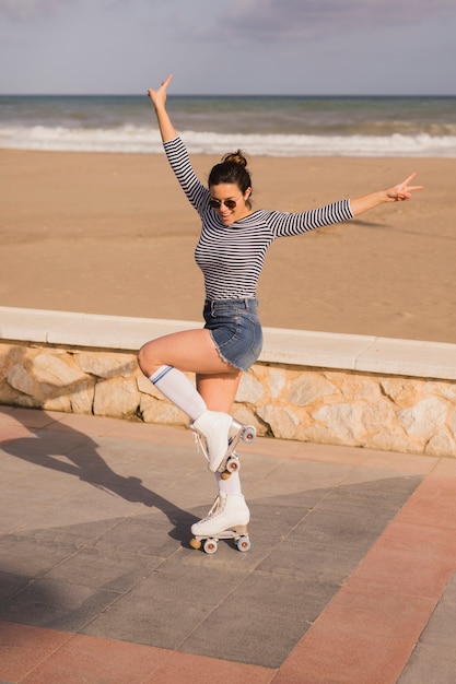 Glimlachende jonge vrouw in rolschaats die vredesteken toont bij strand