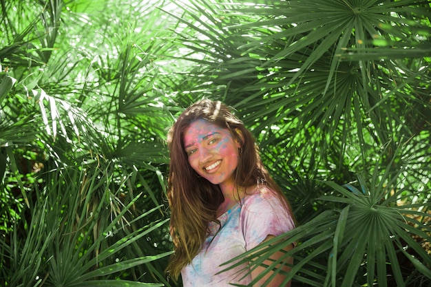 Glimlachende jonge vrouw met holikleur op haar lichaam die zich onder de groene palmbladen bevinden