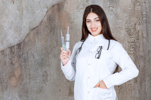 Glimlachende jonge vrouwelijke arts die injecteert met hand op grijze muur