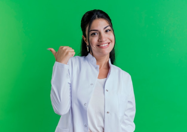 Glimlachende jonge vrouwelijke arts die medische mantel draagt die naar kant kijkt