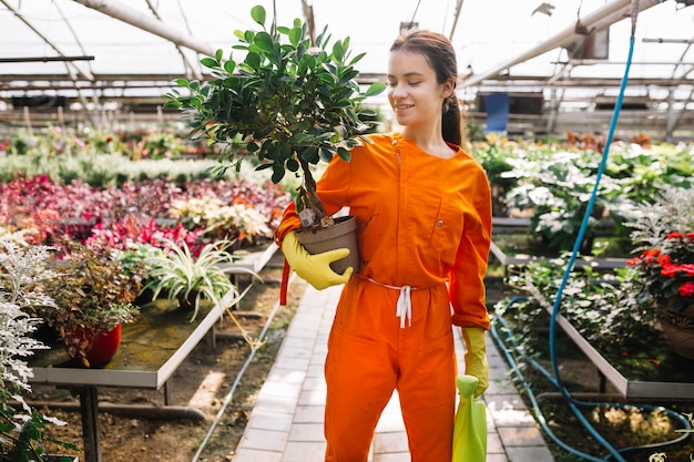 Glimlachende jonge vrouwelijke tuinman die ingemaakte installatie en gieter houden